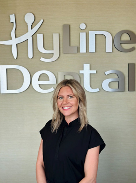 A woman is standing in front of a sign for  Hyloline Dental.