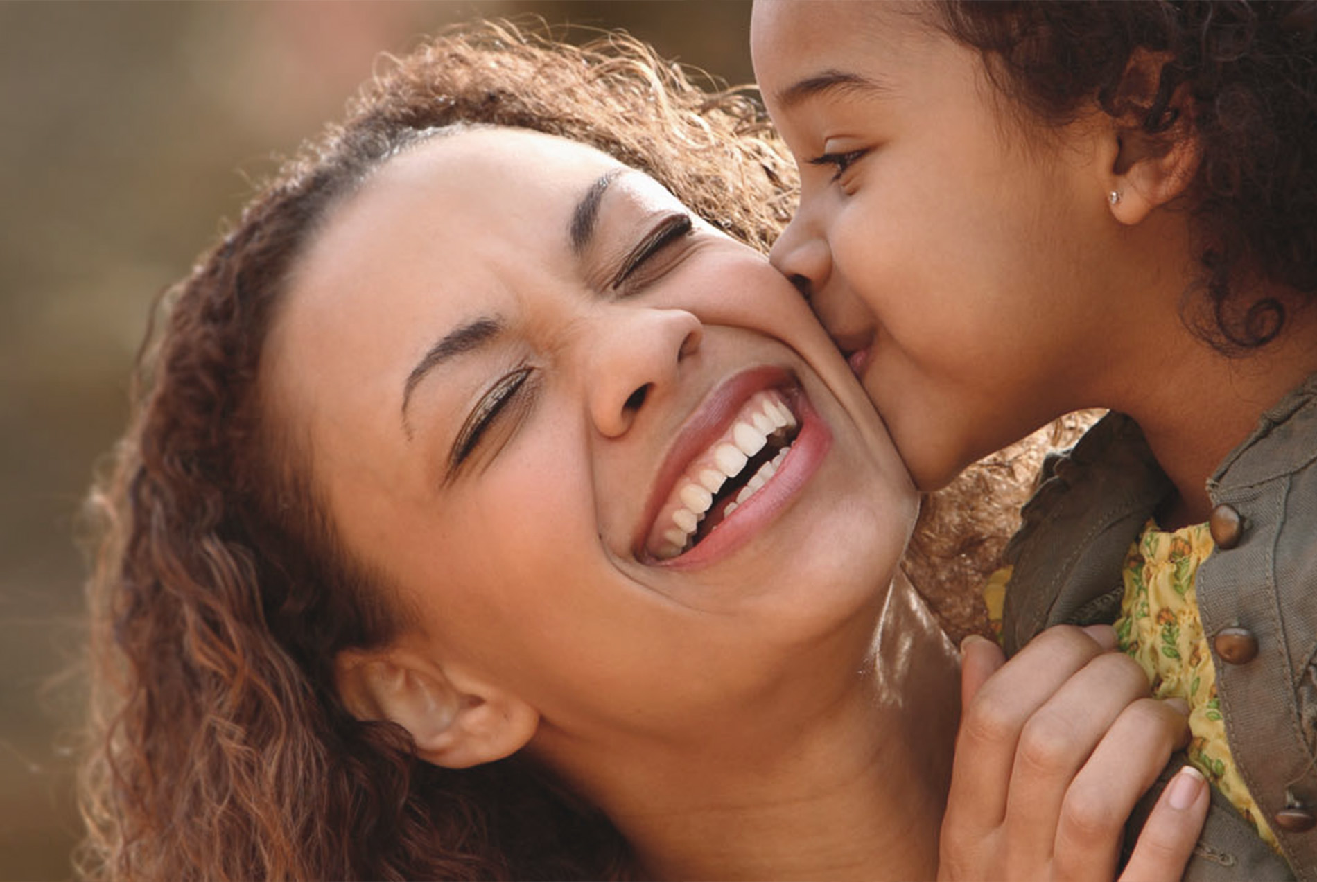 A woman and a child are joyfully sharing a kiss on the cheek, capturing a tender moment of affection between them.