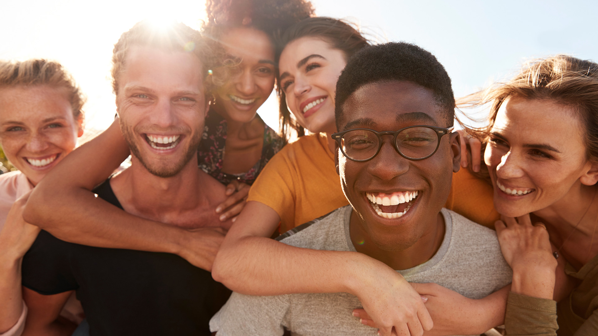 A group of happy individuals celebrating with a hug, set against a sunny background.