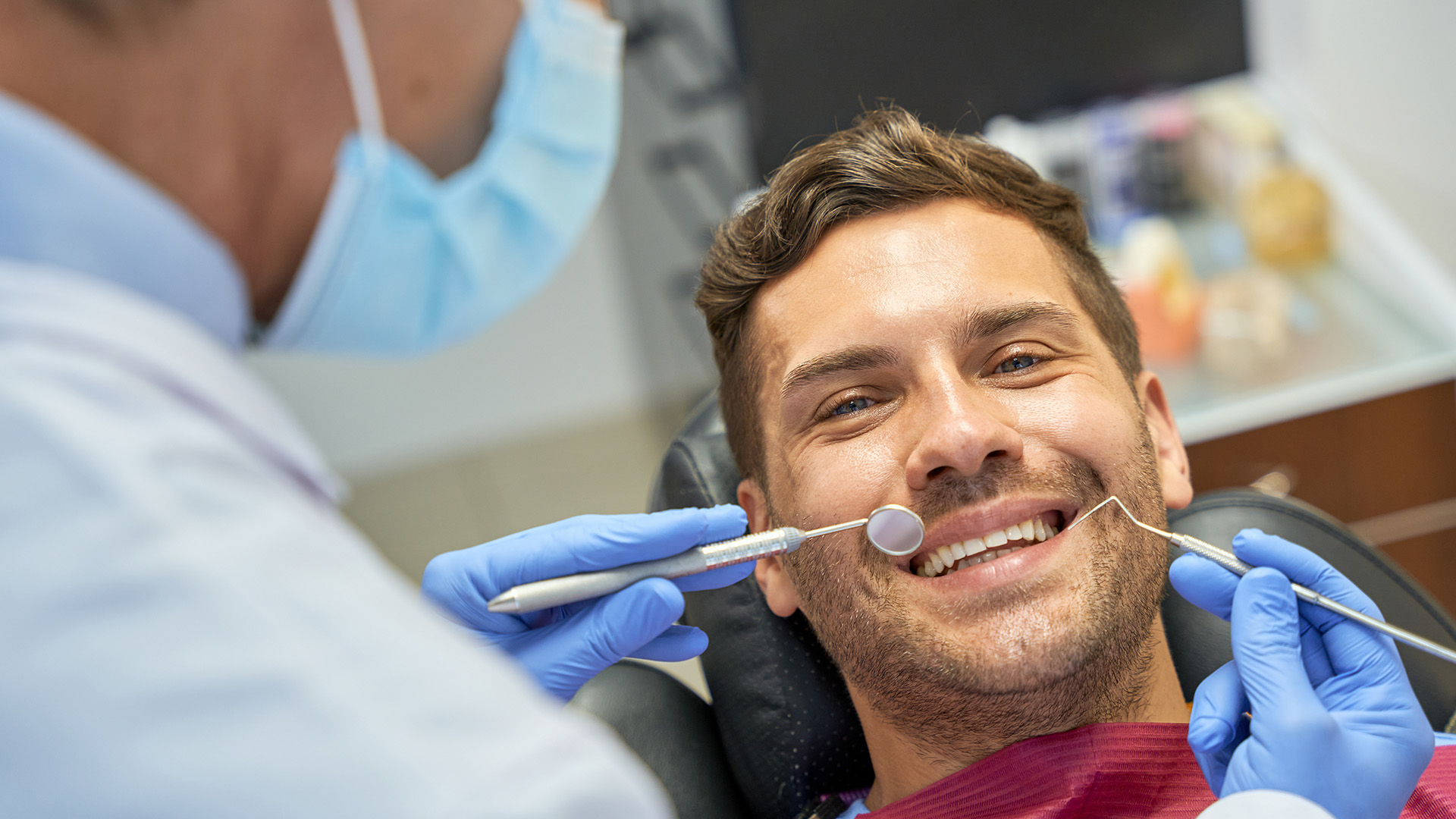 The image shows a man sitting in a dentist s chair, smiling and wearing a mouthguard, while a dental professional is standing behind him, using a drill on his teeth.