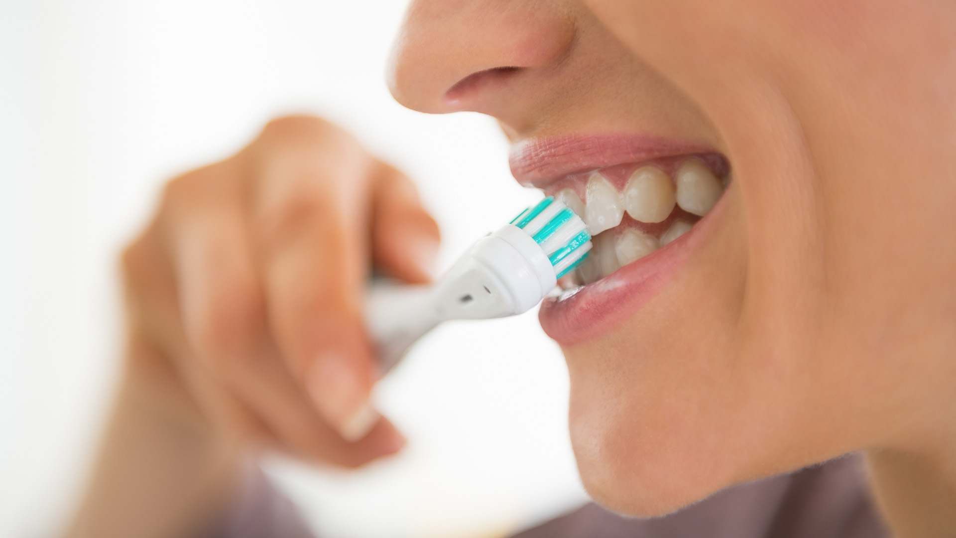 This is a color photograph showing a close-up of a person brushing their teeth with an electric toothbrush. The individual appears to be a woman with her mouth open, and the image captures the action of brushing with the toothbrush in the foreground.