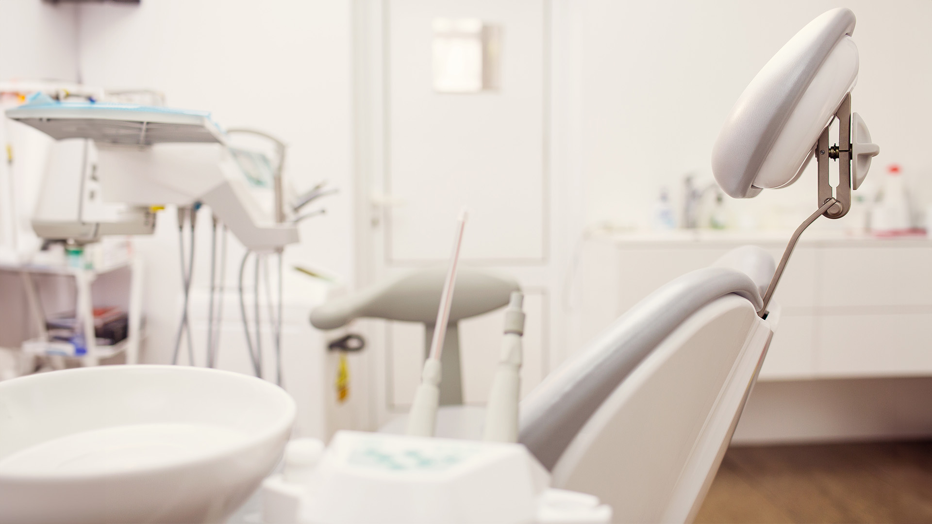 The image depicts a modern dental office interior with a focus on the dental chair and equipment.