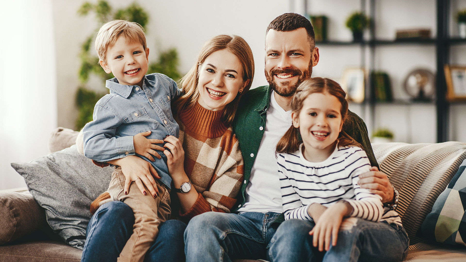 The image shows a family of four, including two adults and two children, posing for a photo in their living room.