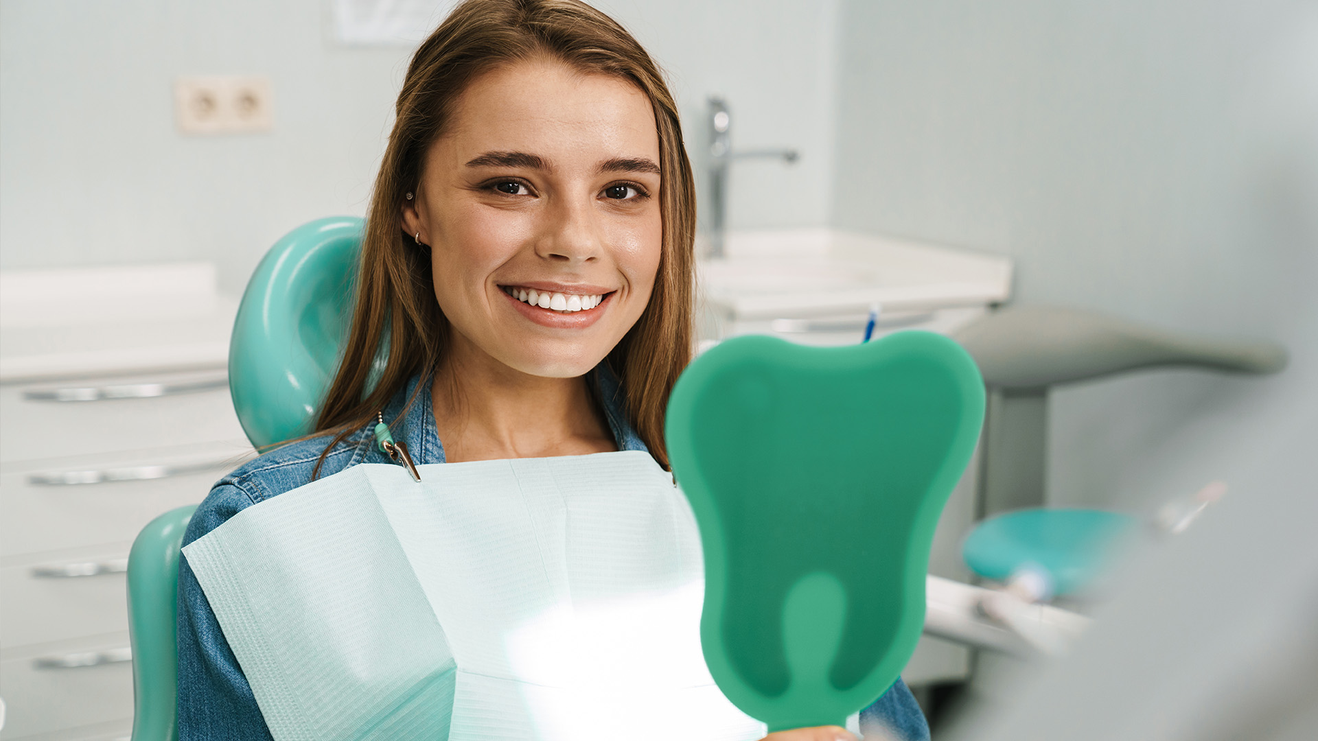 A young woman in a dental office, smiling at the camera while holding a toothbrush.