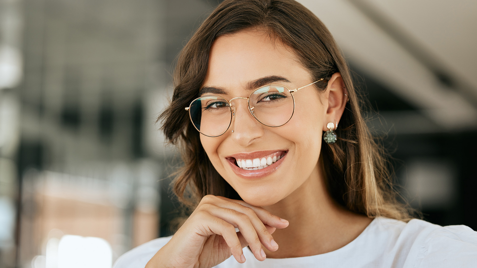 A smiling woman with glasses and a white top, posing against a blurred background.