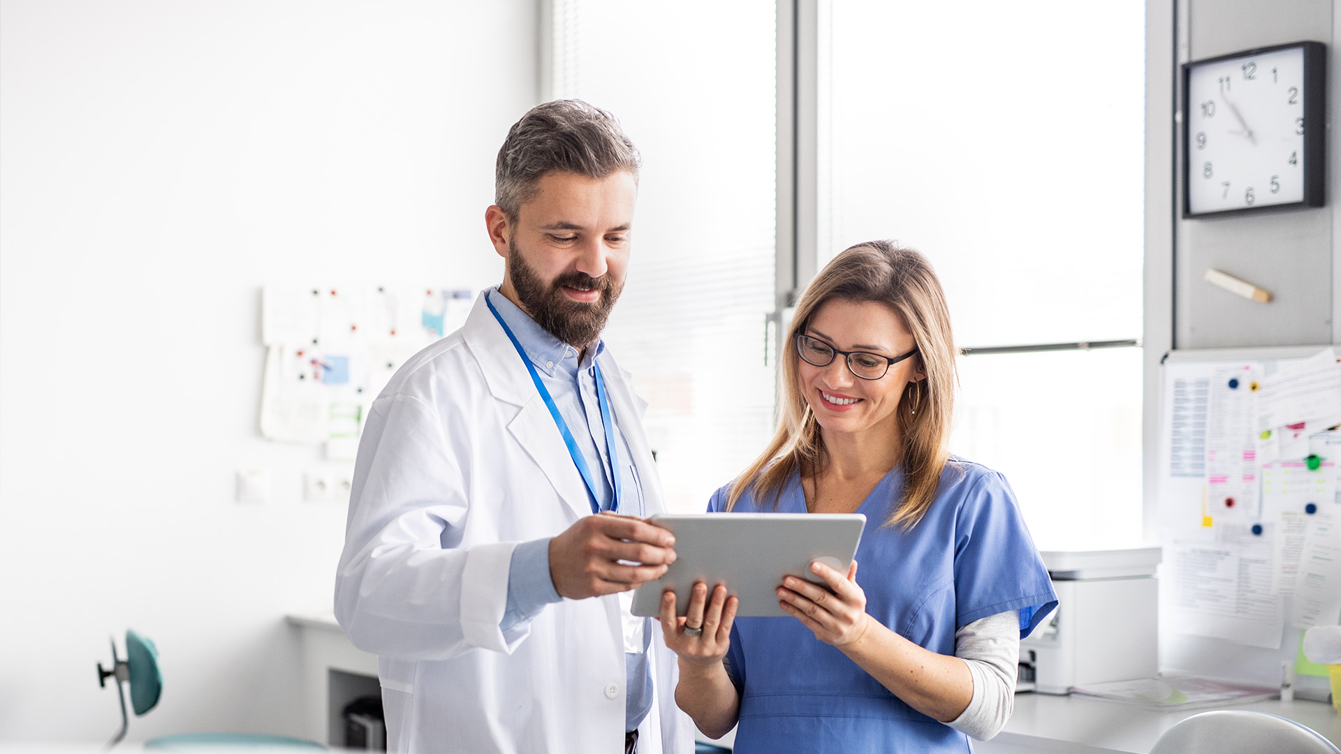 A man and a woman in a medical setting, with the man holding a tablet.