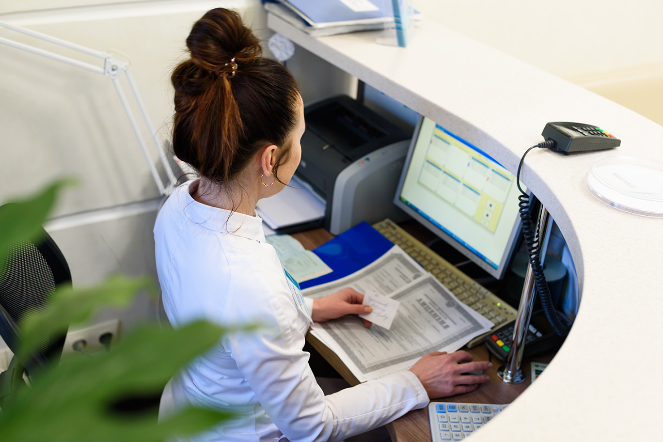 A woman is seated at a reception desk, working on a computer.