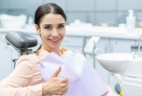 A woman in a dental office, smiling and giving a thumbs-up while seated in a dentist s chair.