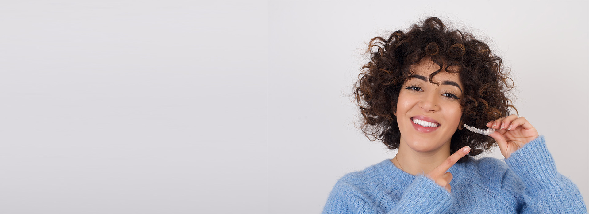 The image shows a person smiling and holding up their hand with fingers spread, against a plain background.