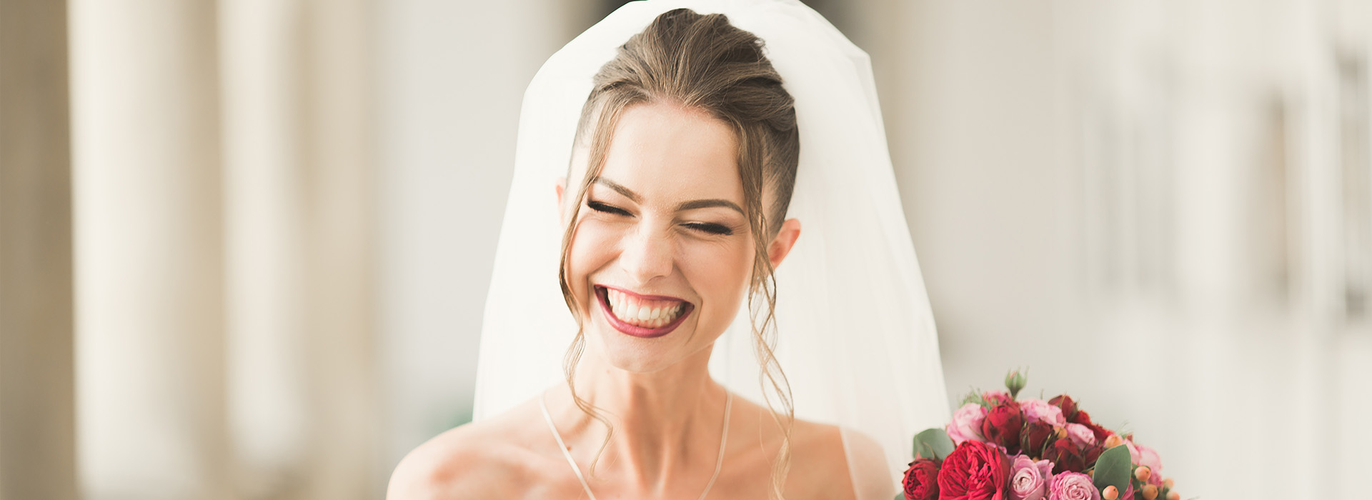 Bride wearing a white veil and holding bouquet, smiling at camera.