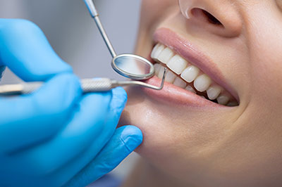 The image shows a person receiving dental care, with a dental professional performing a procedure on their teeth while wearing protective gloves and using a dental mirror.