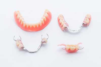 The image shows a collection of dental prosthetics, including upper and lower dentures with visible teeth and gum structures, displayed on a white background.