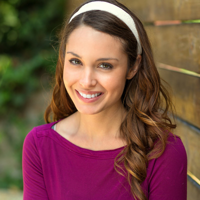 A young woman with long hair, wearing a purple top and a headband, smiling at the camera.