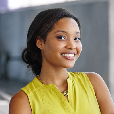 Smiling woman in a bright yellow top, posing against a blurred background.