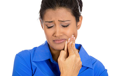 A woman with a concerned expression, looking down at her hand which is holding a toothbrush.