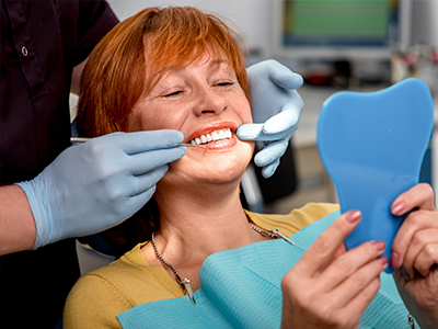 A woman in a dental chair receiving dental care, with a dental hygienist adjusting her mouthpiece.