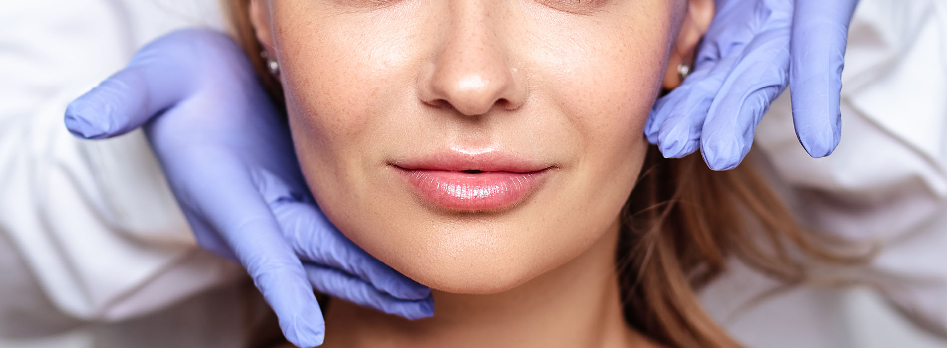 A woman in a medical setting, receiving facial treatment with visible blue gloves and a medical mask.