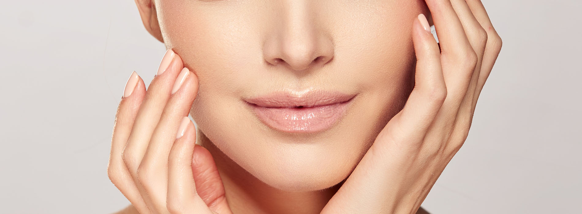 A close-up photo of a woman with a serene expression, holding her face with both hands, showcasing skincare products.