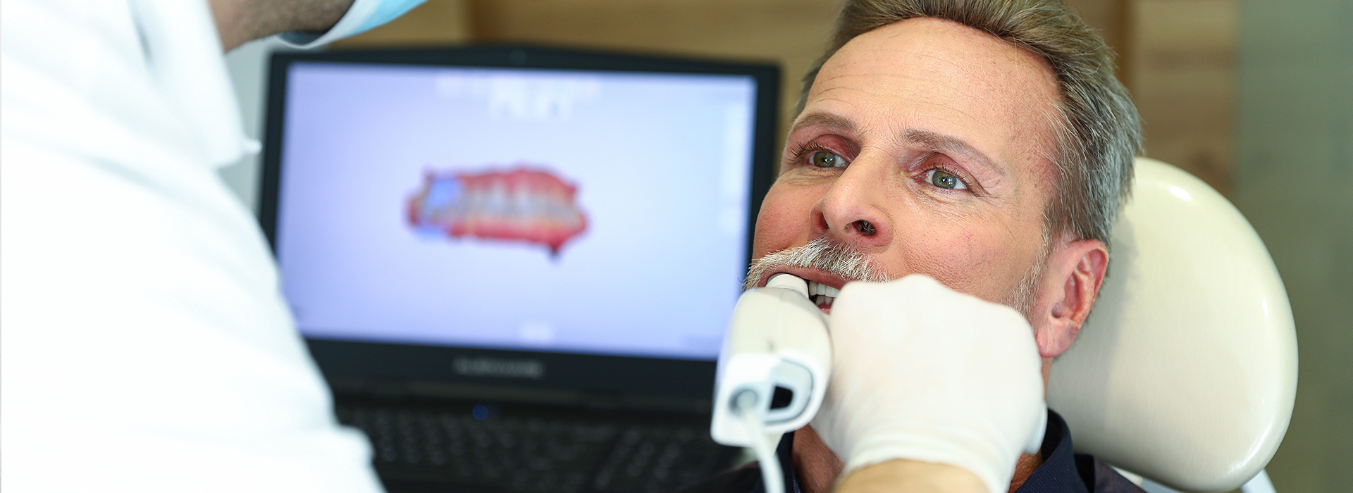 A man receiving dental treatment, with a dentist performing the procedure using a computer-assisted device.