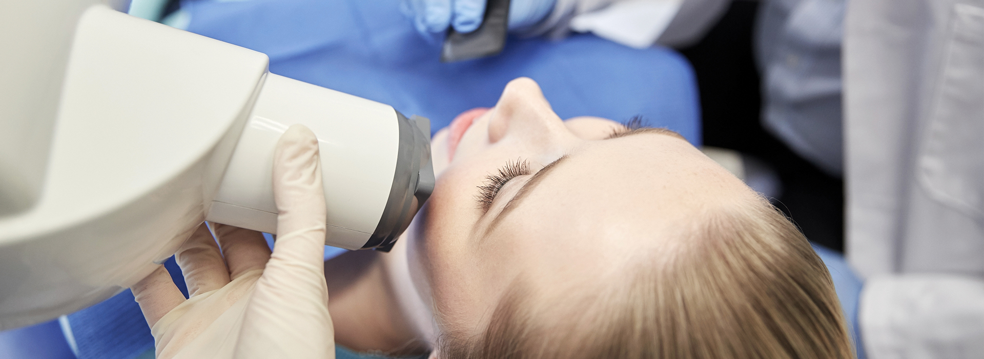 A person receiving a dental examination with a dental mirror and light, while seated in a dental chair.