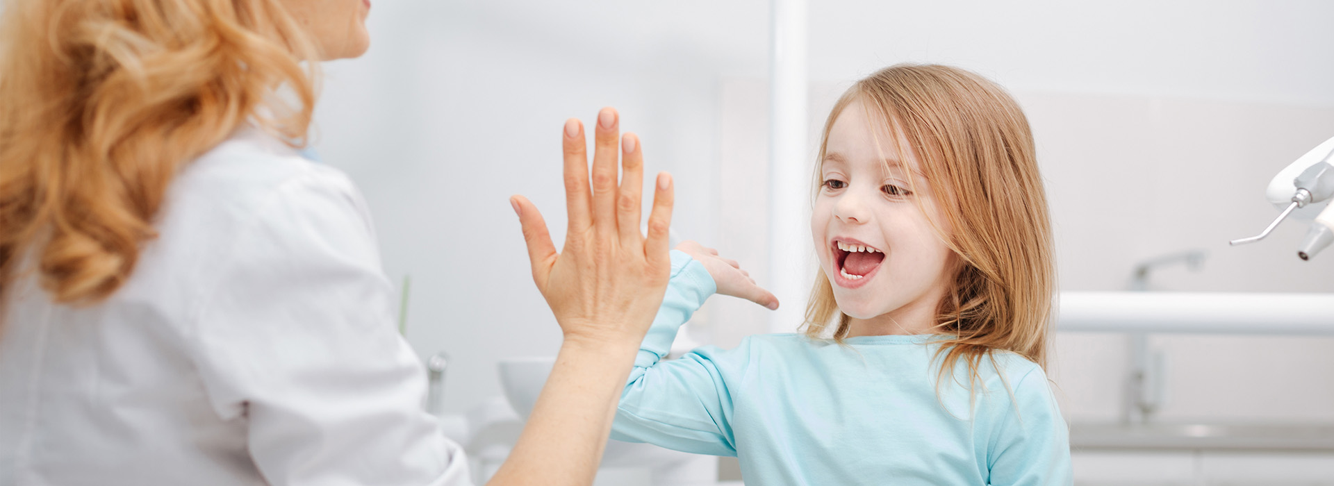 A woman and a young girl are in a dental office, with the woman looking at the child who is smiling.