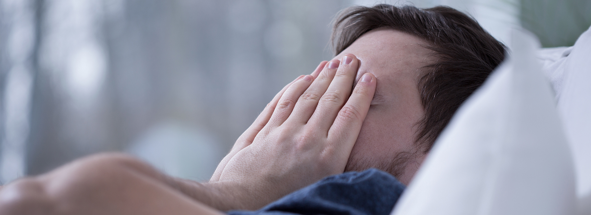 A person lying on a bed with their face covered by their hands, appearing to be in a state of distress or sadness.