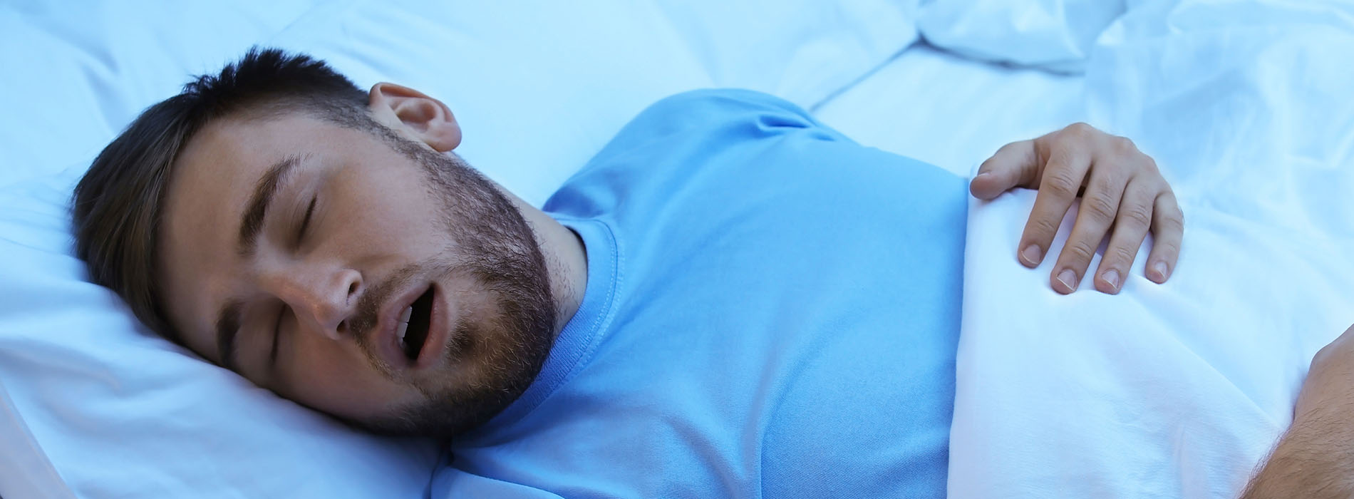 The image shows a man lying in bed, appearing to be asleep or resting with his eyes closed.