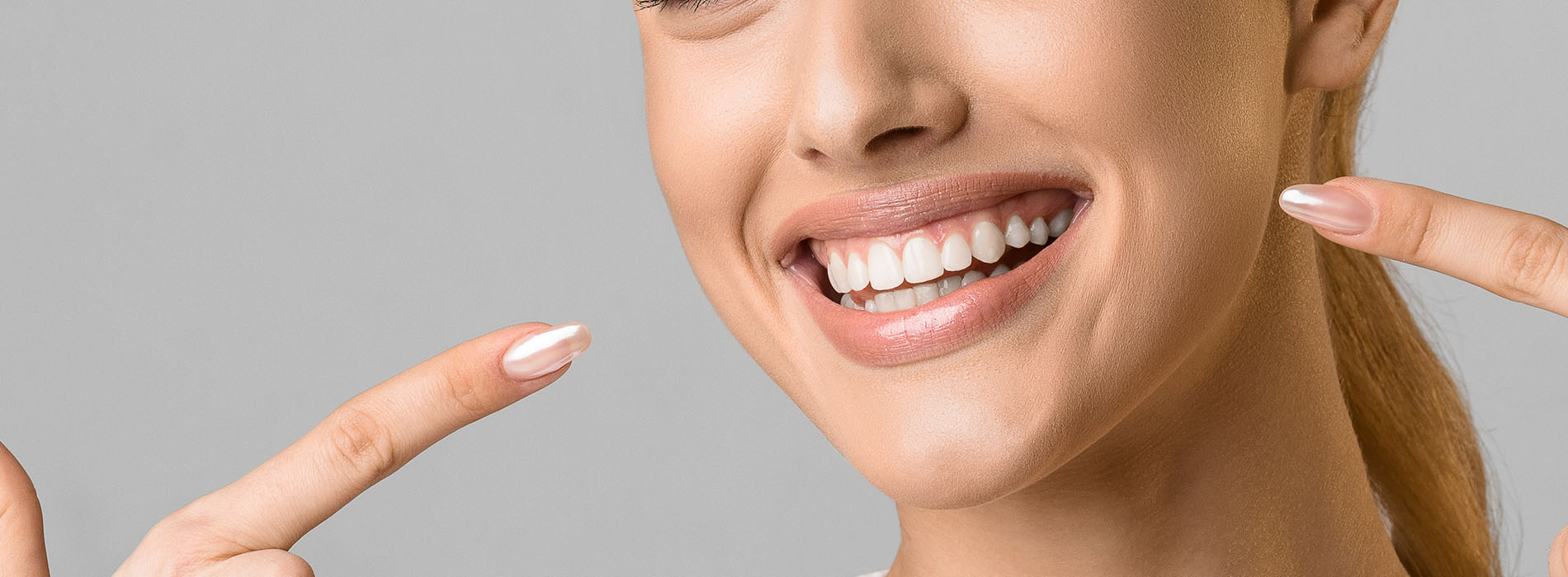 The image shows a smiling woman with her eyes closed, holding up two fingers on each hand, against a neutral background.