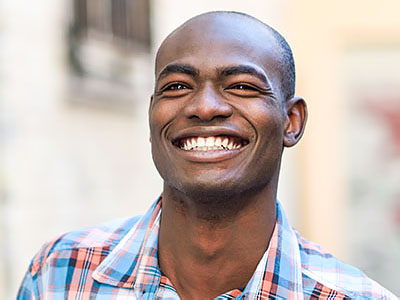 The image shows a smiling man with short hair, wearing a plaid shirt, and posing for the camera.