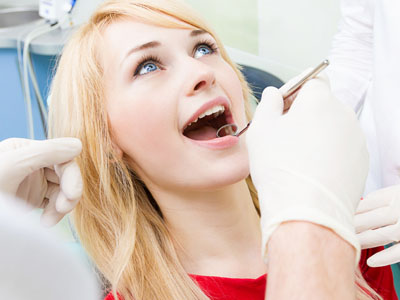 The image shows a woman sitting in a dental chair, receiving dental treatment with a smile on her face.