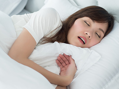 A woman asleep in bed with her eyes closed, wearing a white t-shirt and holding a pillow to her chest.